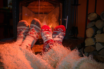 Feets in woollen socks by the Christmas fireplace. Couple sitting neat the fireplace, relaxes by warm fire and warming up their feet in woollen socks.