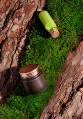 Green glass cosmetic bottle and product mockup in brown and gold colors on textured tree bark and moss podium in rays of sunlight with hard shadows. Mockup for the demonstration of cosmetic products