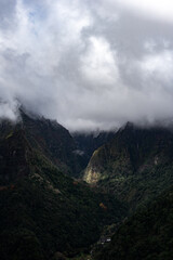 Clouds creating light effects in mountains, dark green mountain forest brightened with sunlight, Madeira