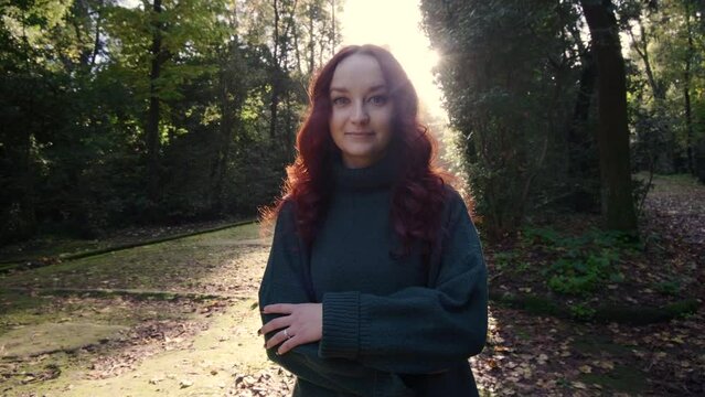 A young girl with red hair and a green sweater looks at the camera. Girl in autumn park
