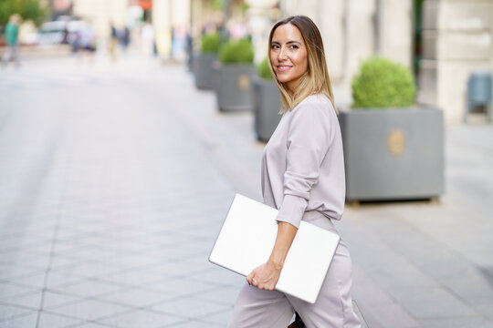 Happy female manager with laptop walking on street before meeting