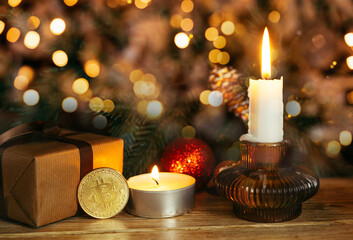 Gold coin bitcoin stands near the christmas decorations on the table with gift box, a spruce branch...