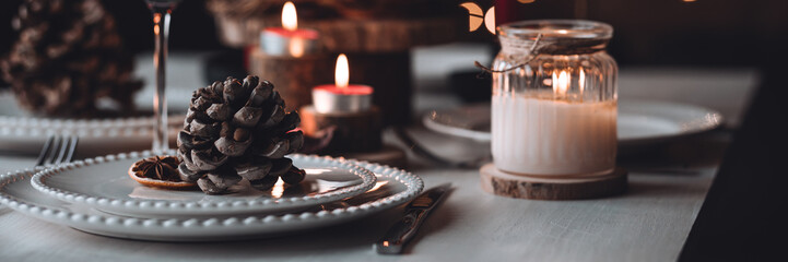 Obraz premium Rustic table decor for Christmas or New Year family dinner. Centrepiece with red candle, dry orange, cone, cinnamon, anise. Zero waste eco-friendly home. Cozy atmosphere, dark background. Banner