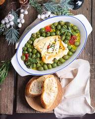 Baked feta cheese with olives, garlic, oil, honey and rosemary in baking dish on a rustic background