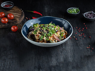 Asian noodles Yakisoba with pork meat in a bowl on wooden dark tabletop.