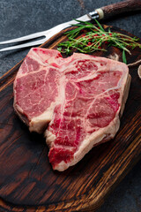 Big Porterhouse beef steak raw dry-aged on a wooden cutting board with grilling seasonings and a meat fork