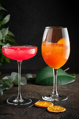 Two bright colored tropical cocktails on a dark background with palm leaves