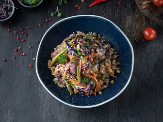 Vegan Fried Rice in black bowl at dark wooden background. Top view