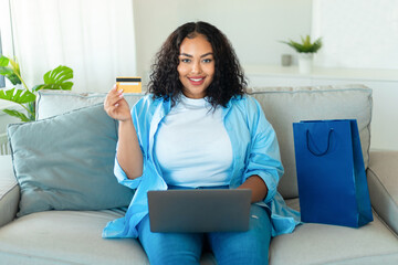 E-commerce concept. Happy black oversize woman using laptop and showing credit card, shopping...