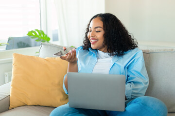 Portrait of young black chubby woman using laptop and talking on speakerphone, dictating voice...