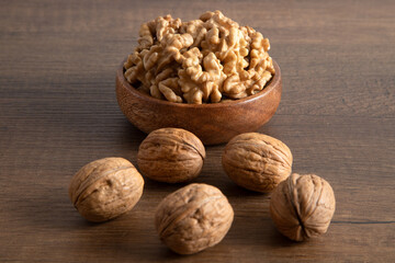 Peeled walnuts and whole walnuts in wooden bowl
