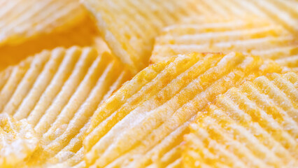 Yellow crispy ridged potato chips close up. Food background, banner, header, wallpaper.
