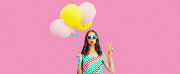 Portrait of beautiful young woman with bunch of colorful balloons blowing her lips sends air kiss wearing on background