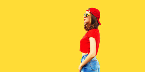 Portrait of stylish young woman wearing red baseball cap looking away isolated on yellow background, blank copy space for advertising text