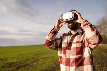 Young man standing in a wheat field at sunset in virtual reality glasses