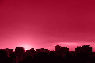 Fototapeta na wymiar Silhouette of city at sunset. Sun is rising over tall buildings. Dramatic sky in sun rays. Urban landscape at dawn. Copy space. Color of the year 2023 - Viva Magenta