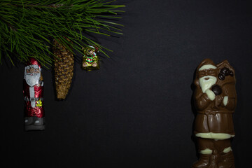 photography of chocolate Santa Claus from of dark and white chocolate on black background and green pine branch whis a New Year Christmas toy chocolate bear and St. Nicholas with fir cone