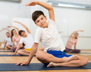 Young boy exercising lotus pose with his family during group yoga training.