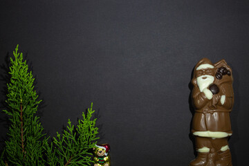 New Year photo - Santa Claus from dark and white chocolate and a Christmas tree with a celebratory bear on a black background