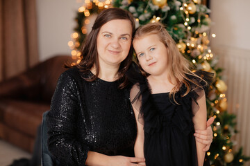 Beautiful mother and daughter with blue eyes. Christmas portraits of a woman in a black dress and a blonde girl. mother daughter resemblance	