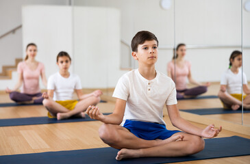 Portrait of smiling teen boy practicing yoga asanas with sister and parents at gym, family health concept