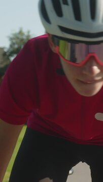 Vertical video of young Caucasian female professional bicyclist during road cycling sprint, continual motion with maximal effort, close up view.