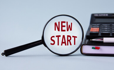 NEW START - words on magnifying glass on a light background with calculator, notepad and pen
