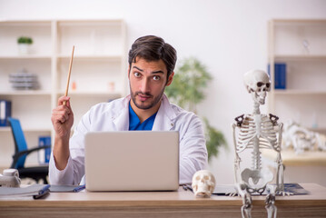 Young male doctor studying human skeleton at the hospital