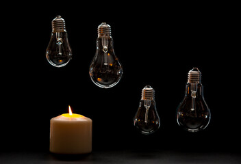 Burning candle near a switched off light bulb in dark home. Blackout, electricity off, load shedding energy crisis or power outage, concept image.