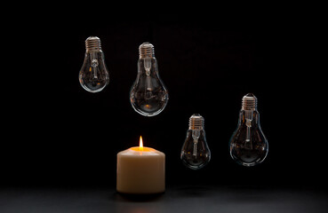 Burning candle near a switched off light bulb in dark home. Blackout, electricity off, load...