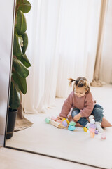 girl plays toys in living room. Montessori wooden toy folded pyramid. Circle, triangle, rectangle...