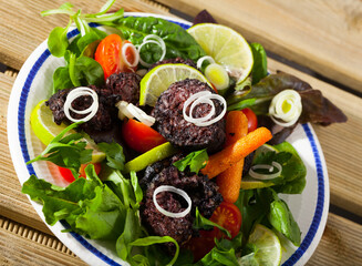 Fried morcilla (blood sausage with rice) served with vegetable salad from tomatoes, carrots and...