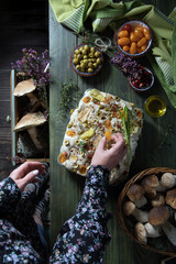 woman decorating italian focaccia bread with vegetables and spices, mushrooms 