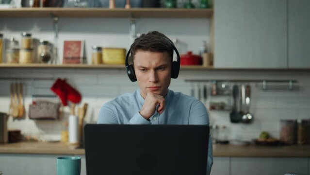 Man listening educational seminar in kitchen with headphones. Student studying.