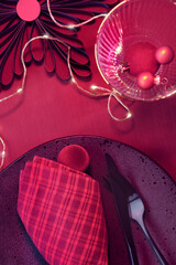 Viva Magenta color of the year 2023. Dark red Christmas background. Monochromatic flat lay with Xmas baubles and garland of electric festive lights on red silk textile background.