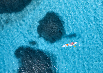 Aerial view of kayak with man in blue sea at sunny day in summer. Man and woman on floating canoe in clear azure water. Sardinia island, Italy. Tropical landscape. Sup board. Active travel. Top view