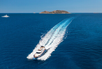 Aerial view of beautiful floating luxury yacht in blue sea at sunset in summer. Sardinia island, Italy. Top view of speed boat, sea coast, transparent water. Travel. Tropical landscape. Yachting 