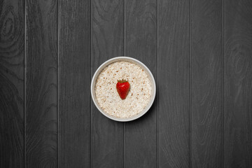 bowl of oatmeal with strawberry on white plate and black wooden background