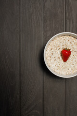 bowl of oatmeal with strawberry on white plate and black wooden background