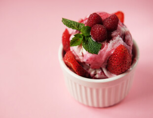 Bowl of pink strawberry ice cream and fresh berries isolated on pink background.