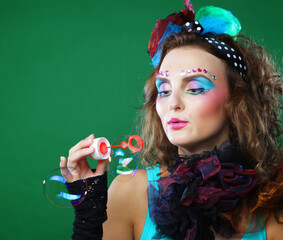 Young woman with creative make-up blowing soap bubbles over green background. Doll style.