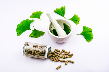 Pills and fresh green ginkgo biloba leaves, mortar and pestle on white background. Natural herbal...
