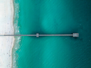 Aerial top down view of wooden pier and white sandy beach in Florida.