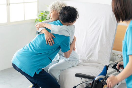 高齢者を介護ベッドから車椅子に移乗させる介護士