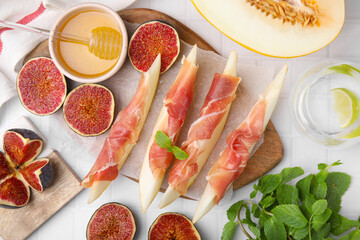 Tasty melon, jamon and figs served on white tiled table, flat lay
