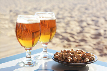 Glasses of cold beer and pistachios on table outdoors