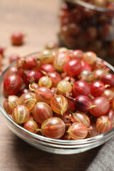 Bowl of fresh ripe gooseberries on wooden table, closeup