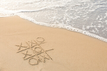 Tic tac toe game drawn on sand near sea, space for text