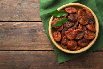 Bowl of tasty apricots and green leaves on wooden table, top view with space for text. Dried fruits