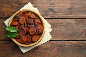 Bowl of tasty apricots and green leaves on wooden table, top view with space for text. Dried fruits